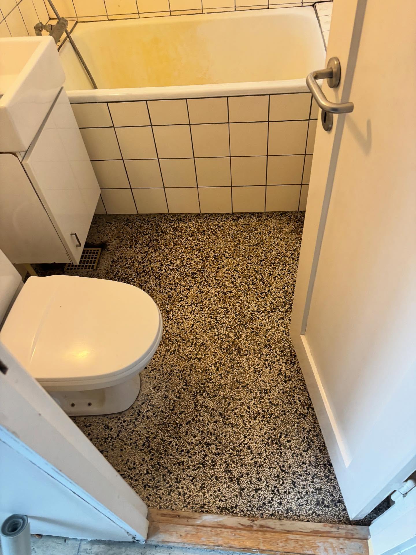 Gammelt terrazzogulv, gulvstående toilet og badekar før nedrivning