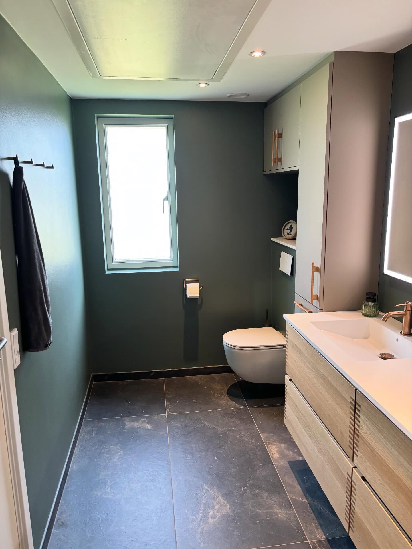 Badeværelse i Valby med grønne vægge, væghængt toilet og vindue