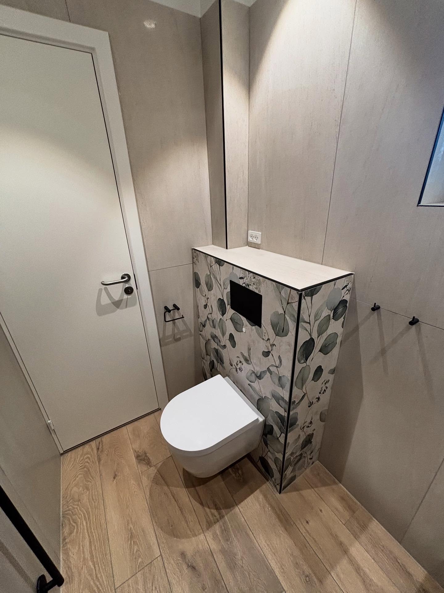 Væghængt toilet med sort betjeningstryk og hylde over forvæggen