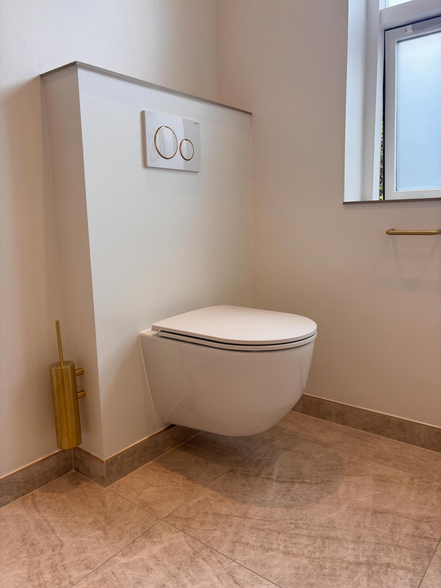 Nærbillede af væghængt toilet med forvæg og messingdetaljer