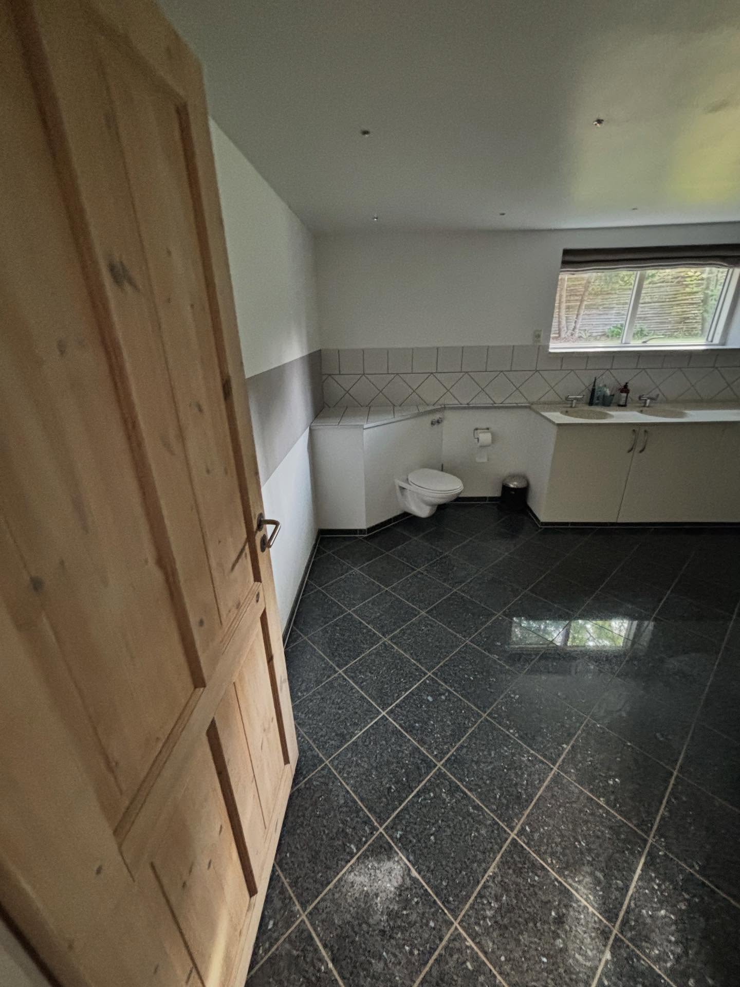 Kælderbadeværelset før renovering set fra døren med mørkt flisegulv