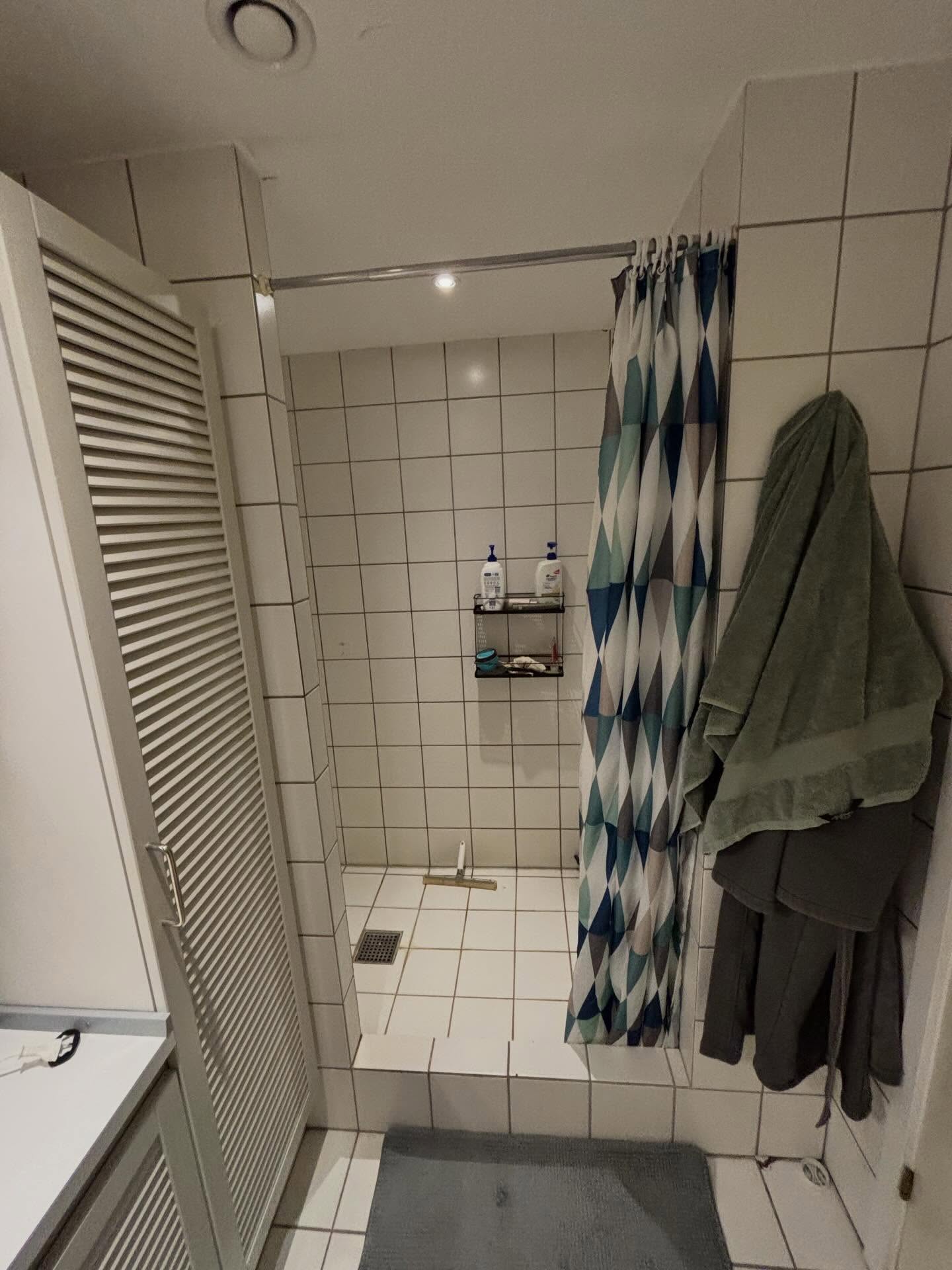 Gammel bruseplads afskærmet med badeforhæng og hvide fliser