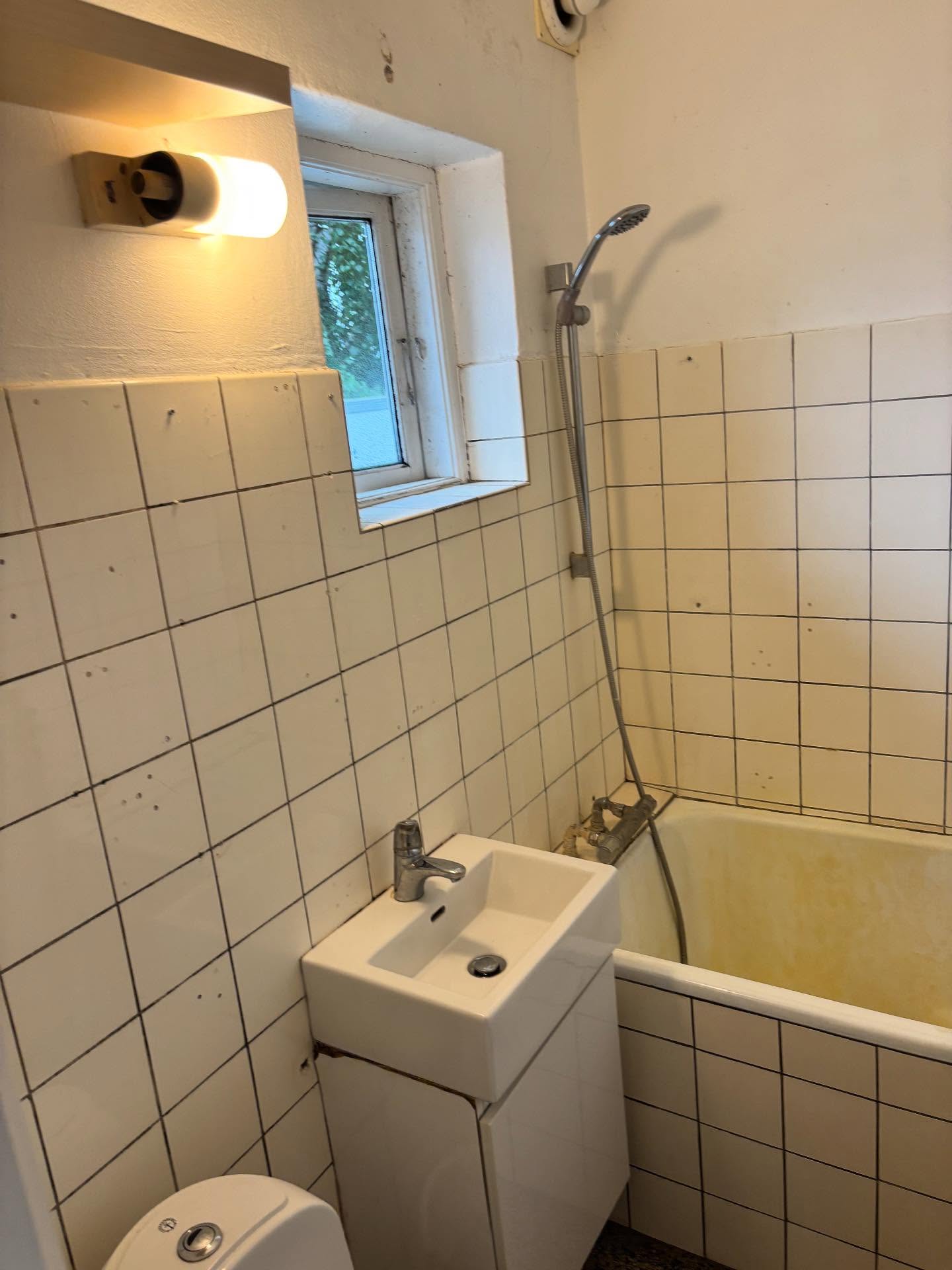Det gamle badeværelse i Rødovre med gult badekar, håndvask og slidte fliser