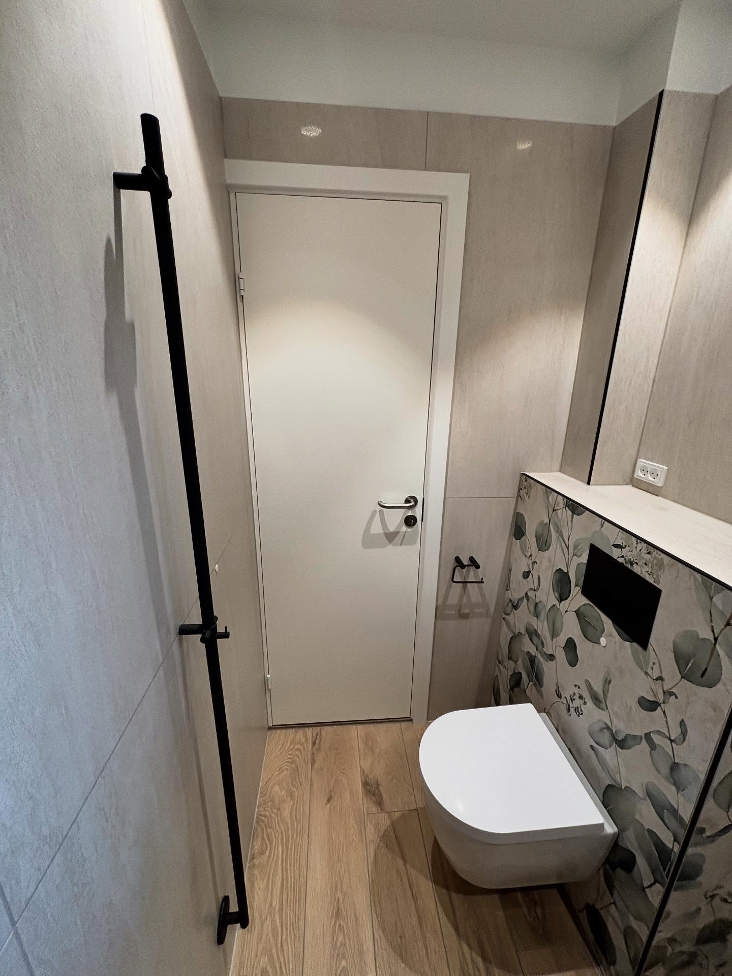 Væghængt toilet med forvæg, sort håndklædestang og træflisegulv
