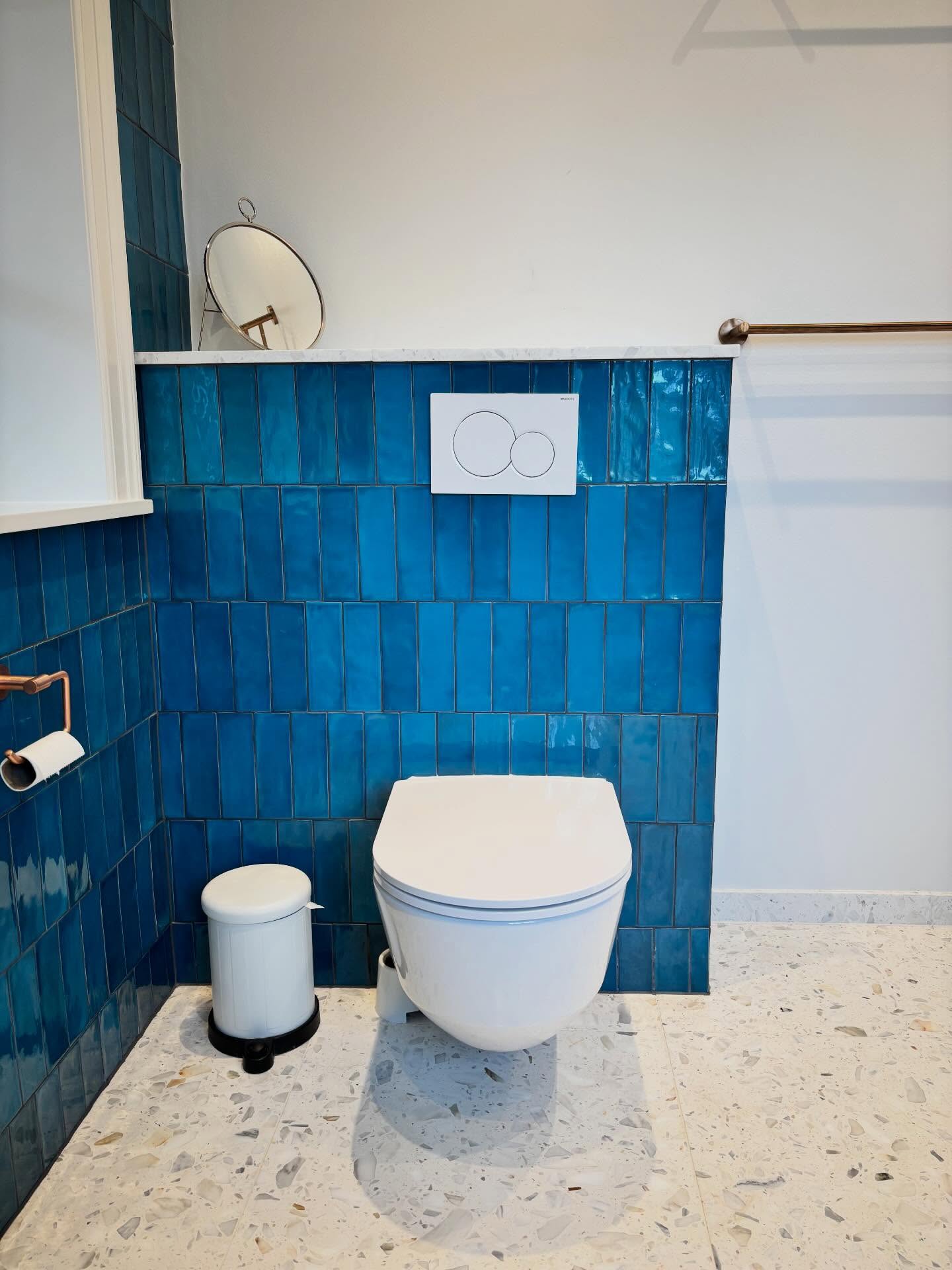 Væghængt toilet med blå fliser, marmorhylde og kobberdetaljer