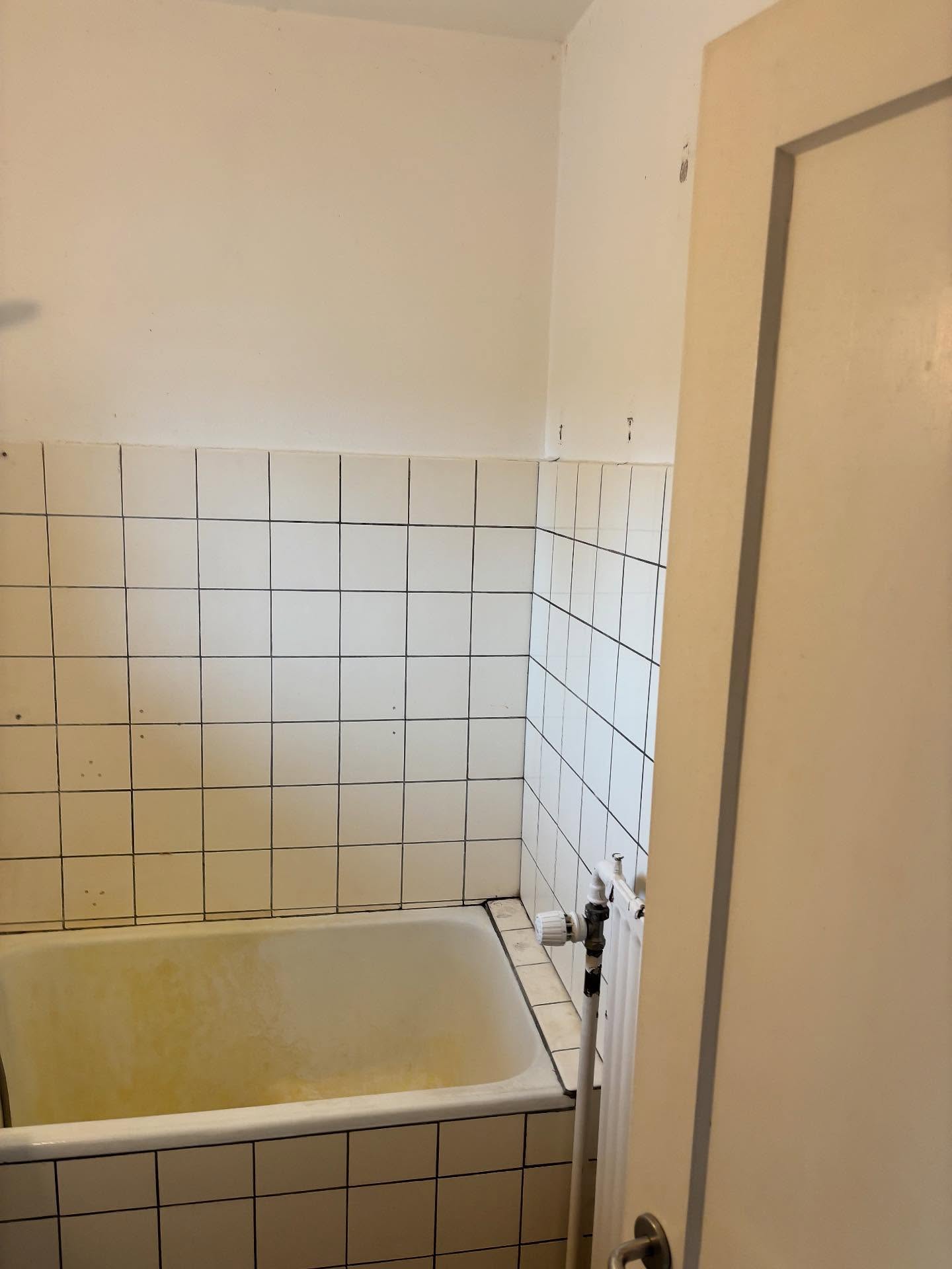 Gult badekar med hvide fliser og mørke fuger før renovering