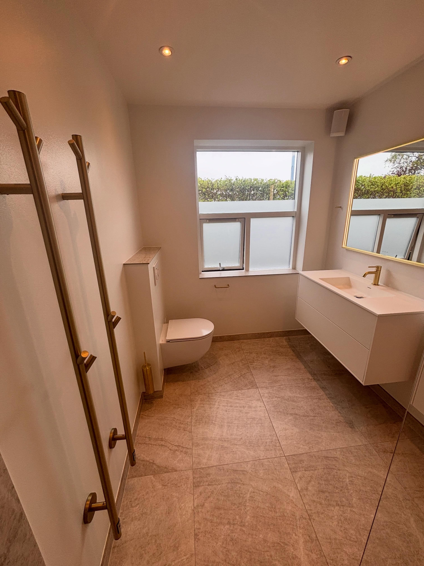 Færdigt badeværelse med væghængt toilet, håndklædetørrer i messing og vaskeplads