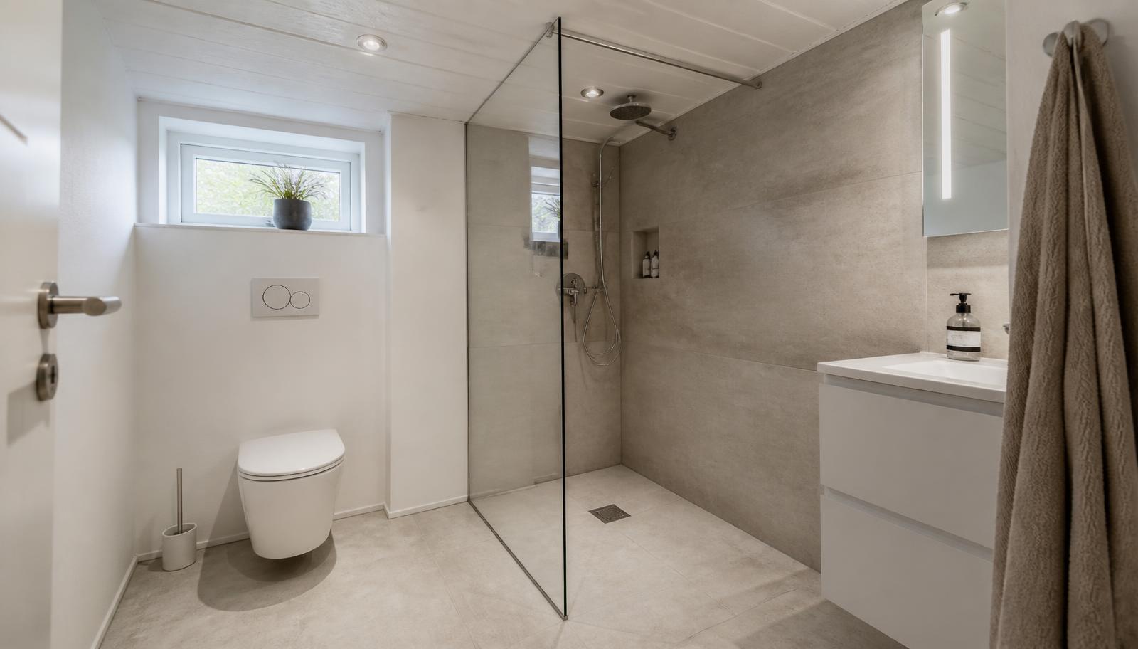 Nyt kælderbadeværelse med walk-in bruser, væghængt toilet og fliser